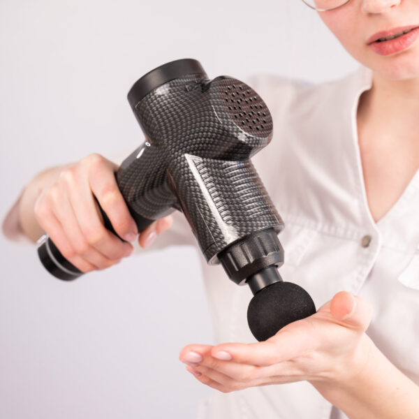 kvinde med massagepistol i haanden ifoert hvid skjorte